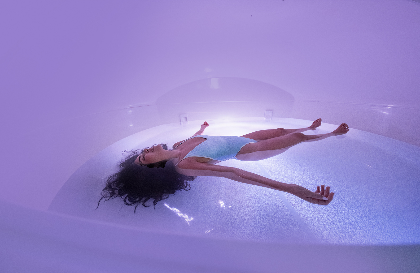 A person floating calmly in a True REST pod bathed in soft purple light.