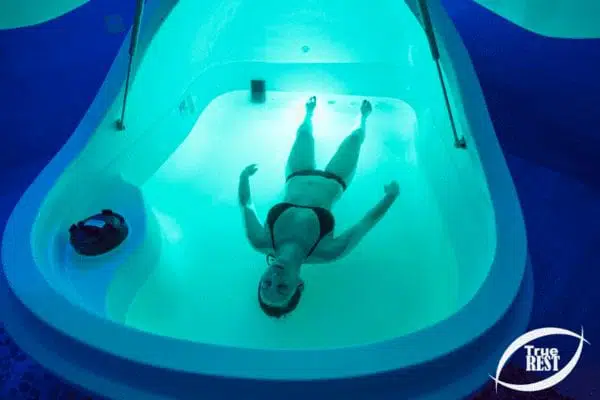 Woman floating weightlessly in a True REST float pod, demonstrating the deep relaxation and sensory deprivation benefits of float therapy.